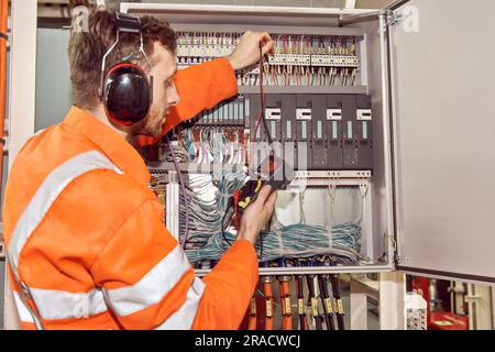 Ingegnere elettrico offshore per il settore petrolifero e del gas che controlla il quadro elettrico con un multimetro. Foto Stock