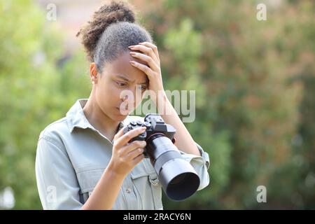 Fotografo nero che si lamenta per aver controllato le foto con la fotocamera in un parco Foto Stock