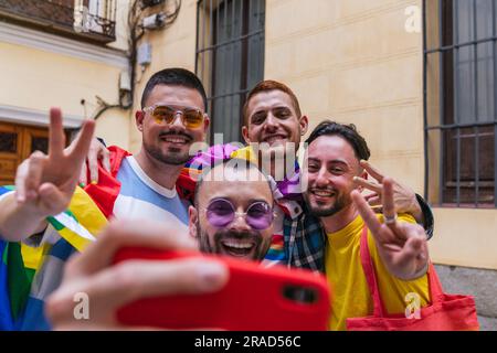 Quattro esuberanti amici gay, che indossano vibranti accessori LGBTQ, catturano la loro felicità in un selfie mentre escono di casa. Foto Stock