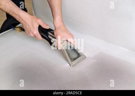 Primo piano della governante con un moderno aspirapolvere per lavaggio e un divano sporco con macchie e detersivo professionale. Foto Stock