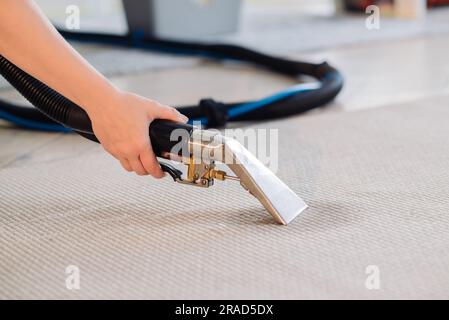 Primo piano della governante con un aspirapolvere moderno e pulizia di tappeti sporchi con macchie e detergenti professionali. Foto Stock
