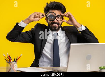 Ricercatore ricercatore scienziato uomo d'affari che lavora in ufficio con lente d'ingrandimento vicino al viso guardando in macchina fotografica con grande zoomato divertente occhio, la ricerca, l'analisi. Uomo freelance professionista Foto Stock