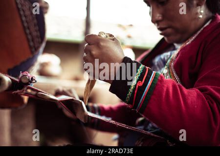 La donna locale in abiti tradizionali trita lana di alpaca con osso Foto Stock
