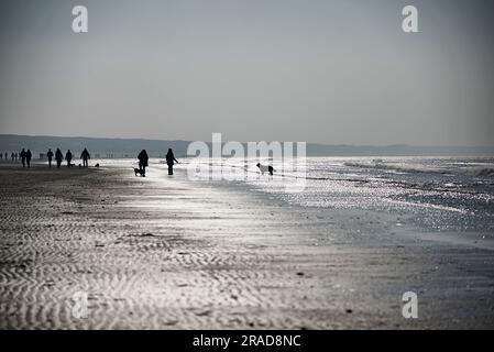 Folle di persone che si divertono a passeggiare lungo la spiaggia sotto il freddo sole invernale Foto Stock