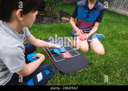 Due ragazzi che giocano a una partita a tac toe con sacchetti di fagioli sull'erba Foto Stock