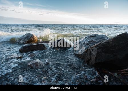 Onde che si infrangono contro grandi rocce sulla riva di un lago durante il giorno. Foto Stock