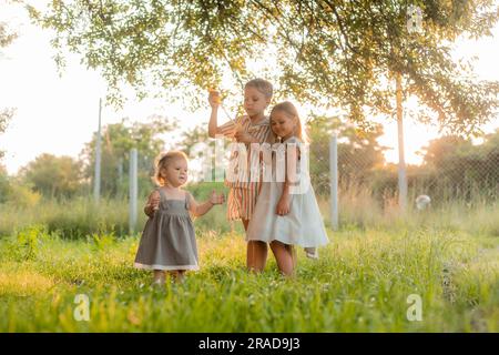 tre bambini piccoli che soffiano bolle di sapone in estate al tramonto in un parco vicino a un albero, spazio per il testo. Foto di alta qualità Foto Stock