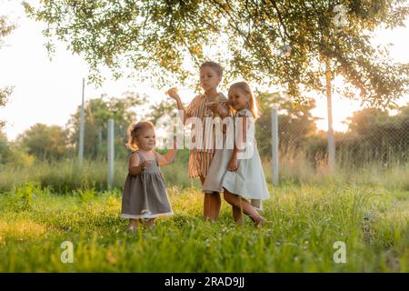 tre bambini piccoli che soffiano bolle di sapone in estate al tramonto in un parco vicino a un albero, spazio per il testo. Foto di alta qualità Foto Stock