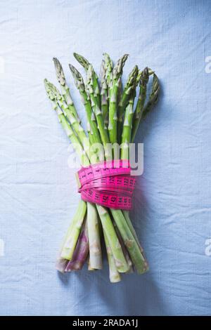 Un fascio di asparagi verdi legato da un nastro a righe rosa Foto Stock