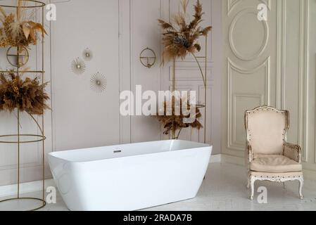 Elegante e luminoso interno del bagno con vasca moderna, fiori secchi, splendidi arredi e divano. Design per la casa. area foto Foto Stock