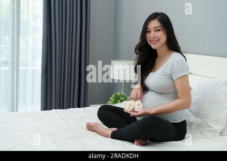 donna incinta con calzini o scarpe per bambini su un letto Foto Stock