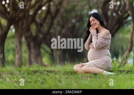 felice donna incinta seduta nel parco Foto Stock