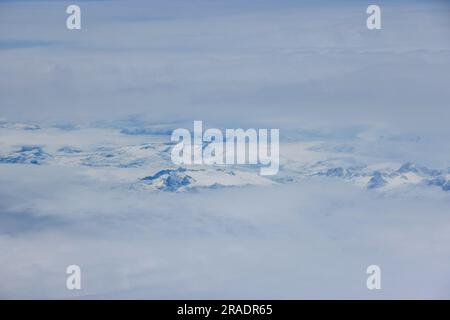 Tra le nuvole emergono maestose vette montuose della Groenlandia adornate da una coperta di neve luccicante Foto Stock