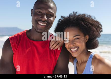 Felice coppia afroamericana in forma che abbraccia e sorride sulla spiaggia soleggiata Foto Stock