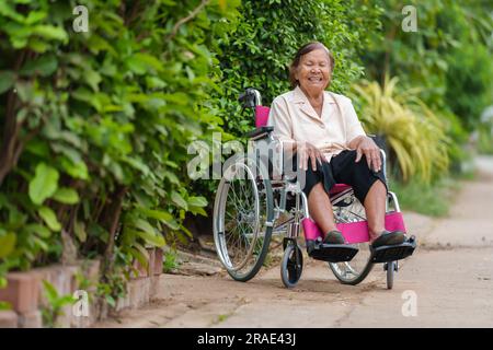 donna anziana felice seduta in sedia a rotelle al parco Foto Stock