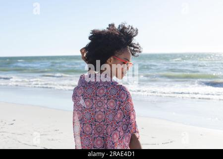 Felice donna afro-americana con occhiali da sole sorridente sulla spiaggia soleggiata in riva al mare Foto Stock