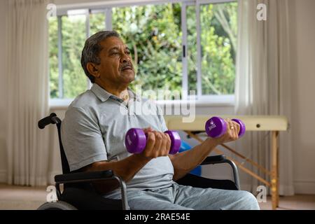 Paziente di sesso maschile birazziale anziano in sedia a rotelle con manubri Foto Stock