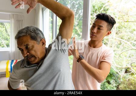 Fisioterapista maschile eterogeneo consigliante e paziente anziano che tende il braccio Foto Stock