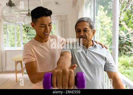 Fisioterapista maschile felice eterogeneo che consiglia e determina un paziente maschile anziano che utilizza manubri Foto Stock