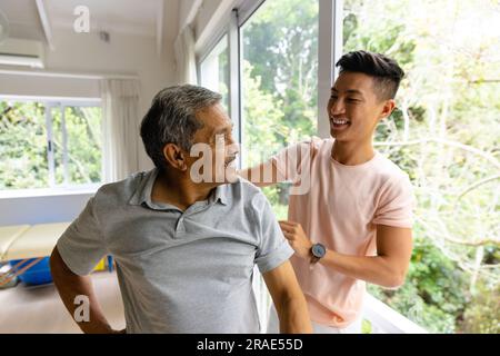 Fisioterapista maschile felice eterogeneo che consiglia e paziente anziano che si esercita Foto Stock