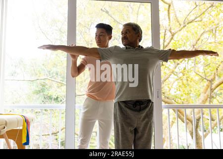 Diversi fisioterapisti maschili consiglianti e pazienti anziani che allungano le braccia Foto Stock