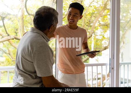 Fisioterapista maschile eterogeneo felice che esamina pazienti di sesso maschile anziani utilizzando la tavoletta Foto Stock