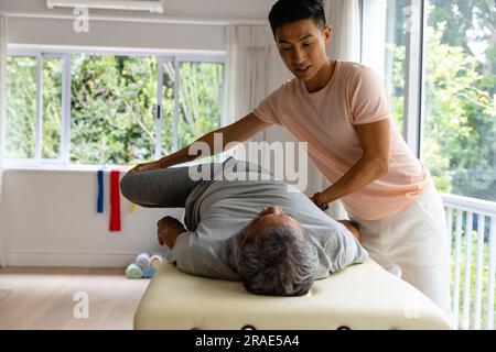 Fisioterapista maschile eterogeneo che consiglia e allungamento del paziente maschile anziano Foto Stock
