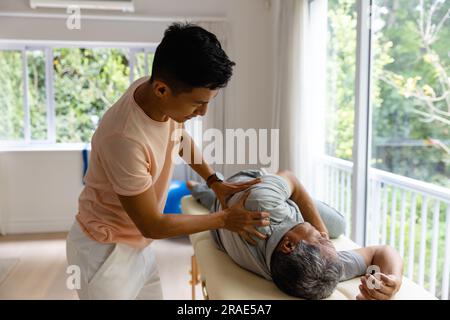 Fisioterapista maschile eterogeneo consigliante e paziente anziano che tende il braccio Foto Stock