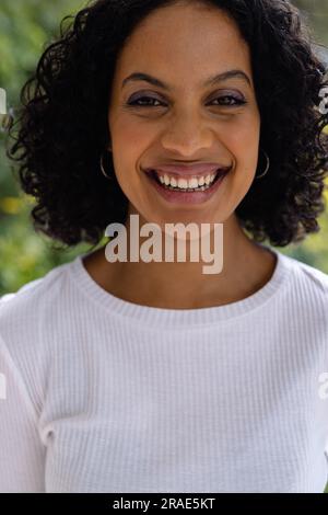 Ritratto di donna birazziale sorridente con capelli scuri ricci davanti alle cime degli alberi Foto Stock