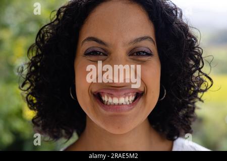 Ritratto di donna birazziale sorridente con capelli scuri ricci davanti alle cime degli alberi Foto Stock