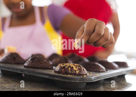 Primo piano di madre e figlia afroamericana che decorano i cupcake in cucina Foto Stock