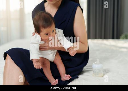 madre che tiene il neonato che ruttava in una camera da letto dopo aver allattato il latte Foto Stock