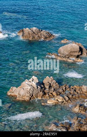 Onde sulla spiaggia rocciosa, riva del mare con onde che si infrangono sulle grandi rocce Foto Stock