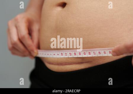 donna che usa un nastro per misurare la cicatrice del cesareo sulla pancia Foto Stock