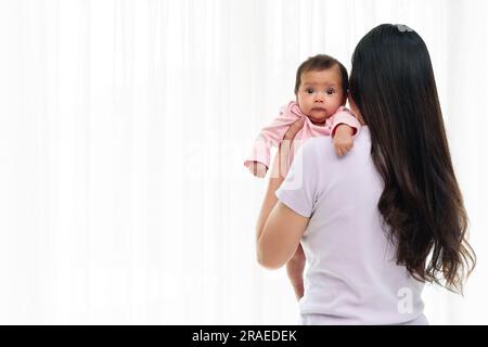 madre che tiene in mano il neonato che rappa dopo aver allattato il latte su uno sfondo bianco della finestra Foto Stock