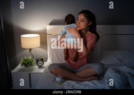 madre che tiene in braccio il neonato che rappa dopo aver allattato il latte su un letto la notte Foto Stock