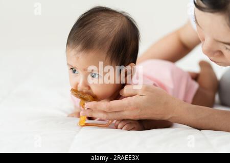 la madre dà un succhietto alla sua bambina su un letto Foto Stock