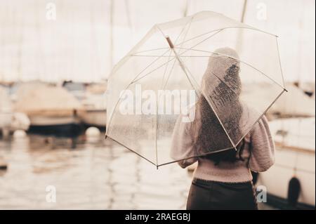 Ritratto all'aperto di una giovane donna sotto la pioggia, che tiene un ombrello, guarda lontano, vista posteriore, immagine in stile retrò Foto Stock