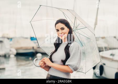 Ritratto all'aperto di una giovane donna sotto la pioggia, con ombrello, immagine in stile moda Foto Stock