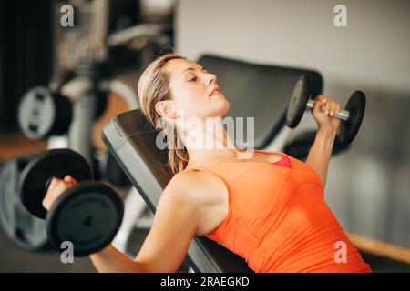 Giovane donna in forma che si allena con i manubri in classe di palestra, vita sportiva sana Foto Stock