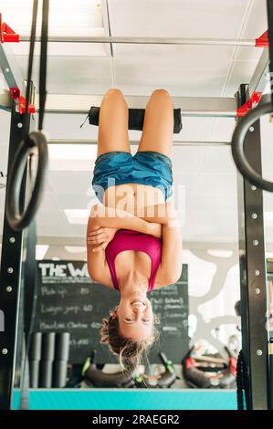 Donna che si allena sulle barre trasversali in una palestra, appesa a testa in giù Foto Stock