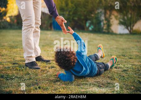 Padre che dà una mano a suo figlio steso a terra Foto Stock