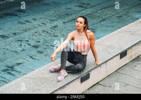 Ritratto all'aperto di una giovane bella donna in forma, che indossa abbigliamento sportivo alla moda, un modello atleta in posa sullo sfondo urbano, moda sportiva Foto Stock