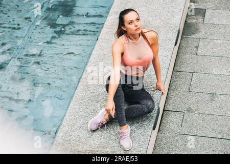 Ritratto all'aperto di una giovane bella donna in forma, che indossa abbigliamento sportivo alla moda, un modello atleta in posa sullo sfondo urbano, moda sportiva Foto Stock