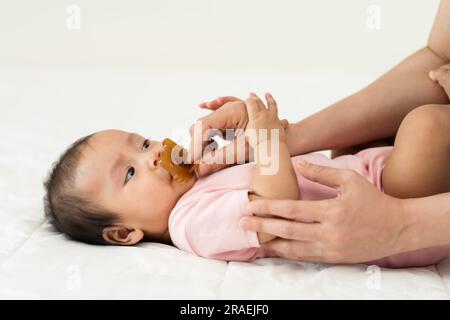 la mano della madre dà un succhietto alla sua bambina su un letto Foto Stock