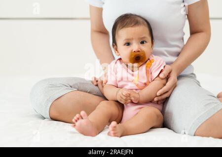 la neonata succhia un succhietto con la madre seduta su un letto Foto Stock