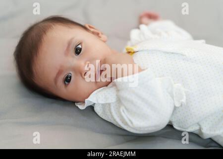 neonato che mette le mani in bocca e succhia le dita su un letto Foto Stock
