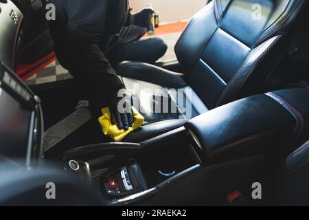 Esperto di dettagli dell'auto inriconoscibile che utilizza un prodotto per la pulizia e un panno in microfibra giallo per pulire il sedile dell'auto in pelle nera. Foto di alta qualità Foto Stock