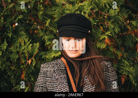 Ritratto all'aperto di una bella giovane donna con i capelli scuri, indossa un blazer a scacchi e un berretto nero Foto Stock