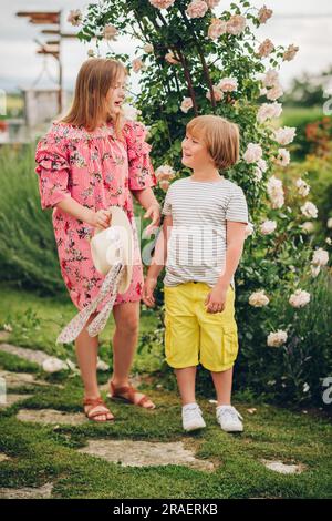 Ritratto estivo di due eleganti bambini in posa nel giardino fiorito in una bella giornata di sole Foto Stock